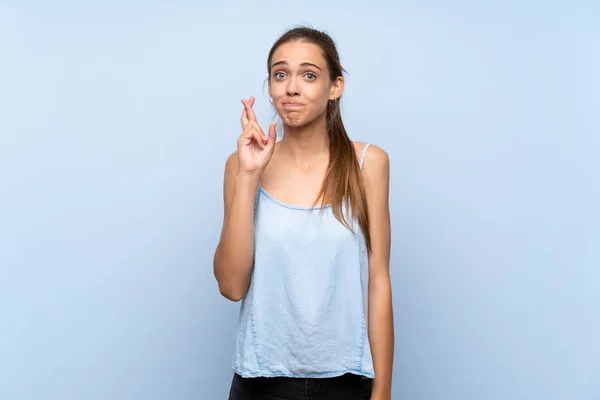 Young woman over isolated blue background with fingers crossing and wishing the best