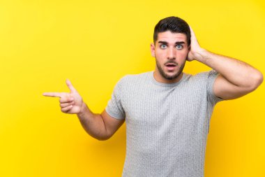 Genç, yakışıklı, izole edilmiş sarı arka planı olan, şaşırmış ve işaret eden bir adam.