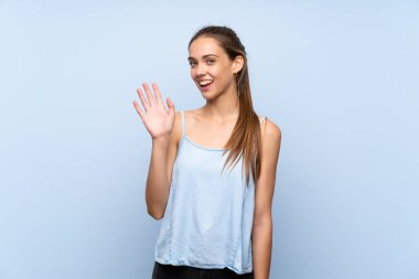 Soyutlanmış mavi arka planda genç bir kadın. Mutlu bir ifadeyle selamlıyor.