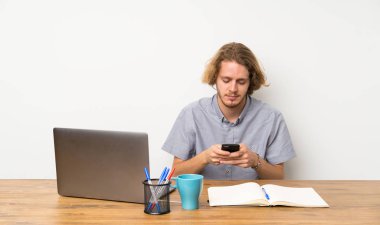 Cep ile bir mesaj gönderen bir laptop ile sarışın adam