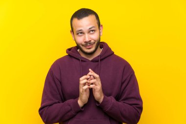 Sarı duvar üzerinde sweatshirt ile Kolombiyalı adam bir şey entrika
