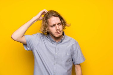 Başını çizerken şüpheleri olan izole sarı arka plan üzerinde Blonde adam