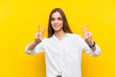 Sarı arka planda genç bir kadın gülümsüyor ve zafer işareti gösteriyor.