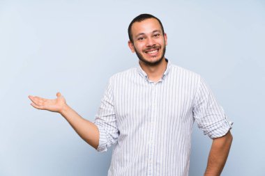 Bir reklam eklemek için palmiye üzerinde izole mavi duvar tutan boşaltmak hayali üzerinde Kolombiyalı adam