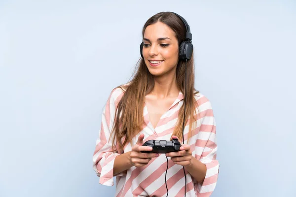 Young woman playing with a video game controller over isolated blue wall smiling a lot
