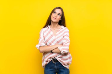 İzole edilmiş sarı arka planda genç bir kadın gülümserken yukarı bakıyor