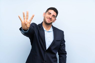 Yakışıklı adam izole edilmiş mavi arka planda mutlu ve parmaklarıyla dört sayıyor.