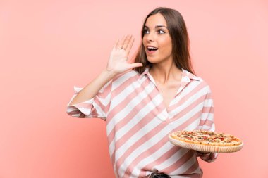 Genç kadın ağzı tamamen açık bağırarak izole pembe duvar üzerinde bir pizza tutan