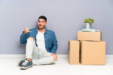 Yakışıklı genç adam telefon jest yapma kutuları arasında yeni evde hareket