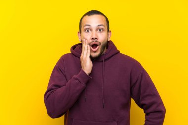Sürpriz ve şok yüz ifadesi ile sarı duvar üzerinde sweatshirt ile Kolombiyalı adam
