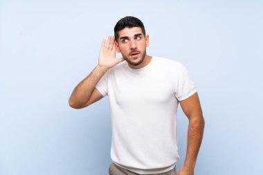 Kafkasyalı yakışıklı adam mavi arka planda elini kulağına koyarak bir şeyler dinliyor.