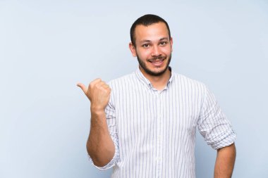 Bir ürün sunmak için yan işaret izole mavi duvar üzerinde Kolombiyalı adam