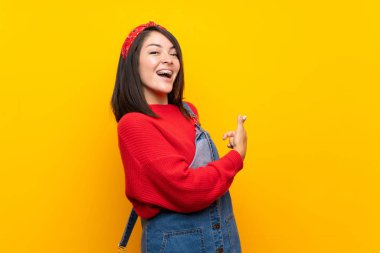 Sarı duvar üzerinde tulum ile genç Meksikalı kadın geri işaret