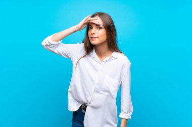İzole edilmiş mavi arka planı olan genç bir kadın bir şeye bakmak için elini uzaklara bakıyor.