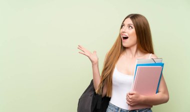 Sürpriz yüz ifadesi ile izole yeşil arka plan üzerinde genç öğrenci kadın