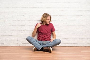 Sarışın adam yorgun ve hasta ifade ile yerde oturuyor