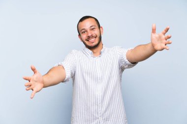 Izole mavi duvar üzerinde Kolombiyalı adam sunan ve el ile gelmek için davet