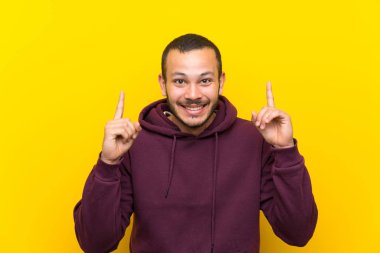 Sarı duvar üzerinde sweatshirt ile Kolombiyalı adam harika bir fikir işaret