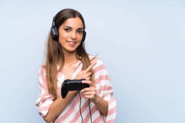 Genç kadın izole mavi duvar üzerinde bir video oyunu denetleyicisi ile oynayan bir ürün sunmak için yan işaret