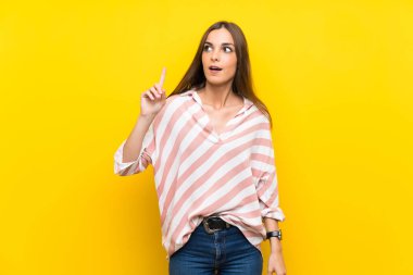 Izole sarı arka plan üzerinde genç kadın bir fikir parmak işaret düşünme