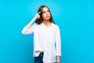 Izole mavi arka plan üzerinde genç kadın kafasına parmak koyarak delilik jest yapma