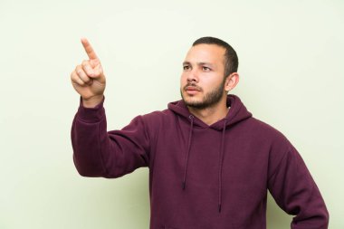 Şeffaf ekrana dokunarak yeşil duvar üzerinde sweatshirt ile Kolombiyalı adam