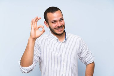 Izole mavi duvar üzerinde Kolombiyalı adam parmakları ile ok işareti gösteren