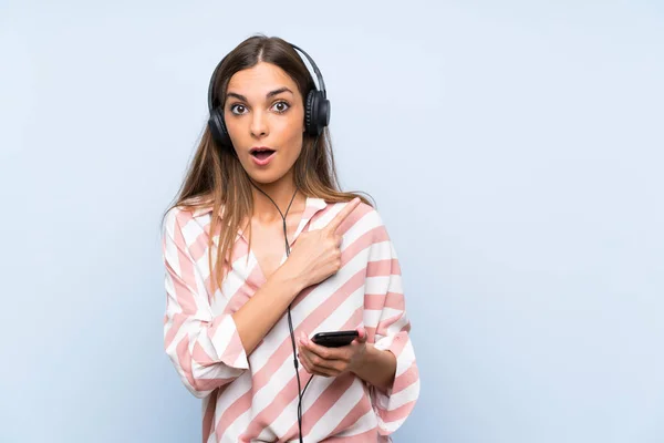 Jonge Vrouw Luisteren Muziek Met Een Mobiele Geïsoleerde Blauwe Muur — Stockfoto