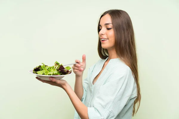 Young woman with salad over isolated green wall