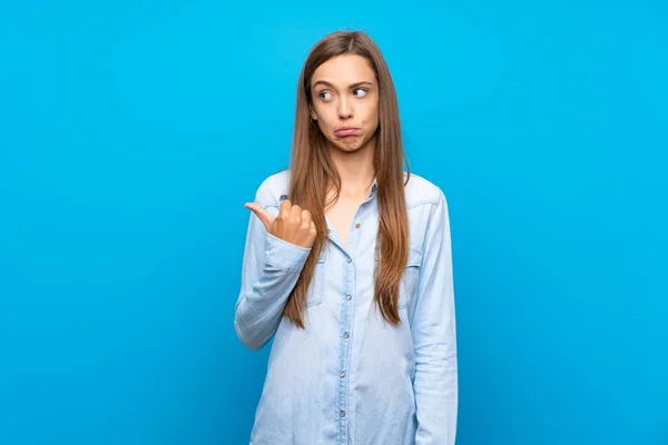 Jonge Vrouw Geïsoleerde Blauwe Achtergrond Ongelukkig Wijzend Naar Zijkant — Stockfoto