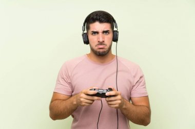 İzole yeşil duvar üzerinde bir video oyunu denetleyicisi ile oynayan genç yakışıklı adam