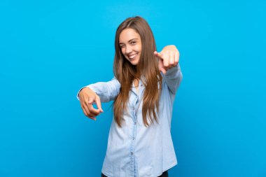Genç kadın üzerinde izole mavi arka plan üzerinde parmak size gülümserken