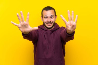 Sarı duvar üzerinde sweatshirt ile Kolombiyalı adam parmakları ile dokuz sayma