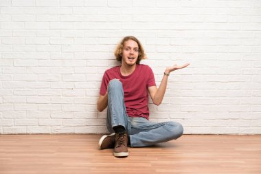 Sarışın adam bir reklam eklemek için avuç üzerinde copyspace hayali tutarak katta oturan