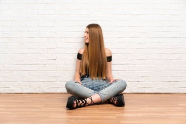 Genç bir kadın yerde oturuyor, yan tarafa bakıyor.