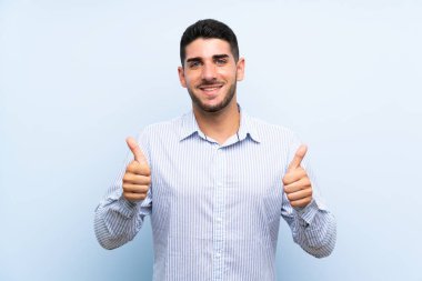 Izole mavi arka plan üzerinde Kafkas yakışıklı adam jest kadar bir başparmak veren