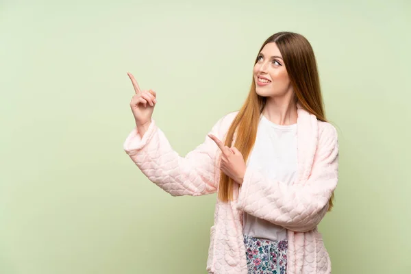 Young woman in dressing gown over green wall pointing with the index finger a great idea