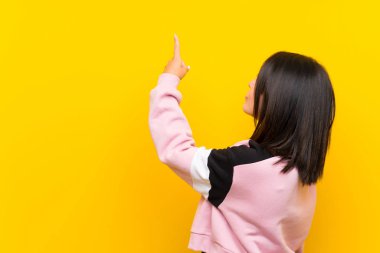 İzmi parmağı ile geri işaret izole sarı arka plan üzerinde Genç Meksikalı kadın