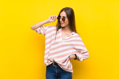 Gözlük ve gülümseyerek izole sarı arka plan üzerinde genç kadın