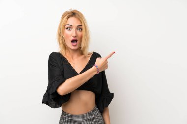 Izole beyaz duvar üzerinde genç sarışın kadın şaşırttı ve yan işaret