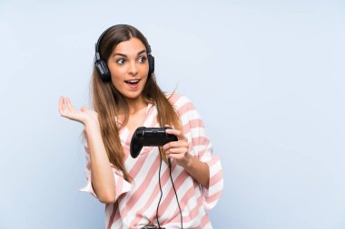 Genç kadın sürpriz yüz ifadesi ile izole mavi duvar üzerinde bir video oyunu denetleyicisi ile oynuyor