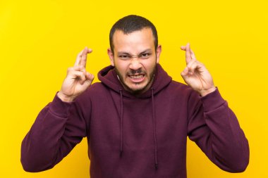 Parmakları geçiş ile sarı duvar üzerinde sweatshirt ile Kolombiyalı adam