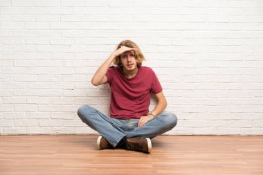 Sarışın adam bir şey bakmak için el ile uzak lara bakarak yerde oturan