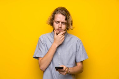 Izole sarı arka plan düşünme ve bir mesaj gönderme üzerinde Blonde adam