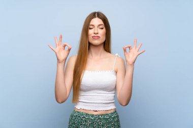 Zen pozunda soyutlanmış mavi arka planı olan genç bir kadın.