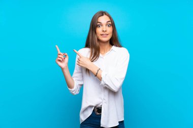 Izole mavi arka plan üzerinde genç kadın korkmuş ve yan işaret