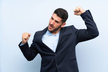 Yakışıklı adam izole edilmiş mavi arka planda zaferi kutluyor