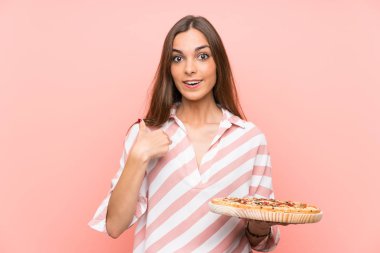 Genç kadın sürpriz yüz ifadesi ile izole pembe duvar üzerinde bir pizza tutan