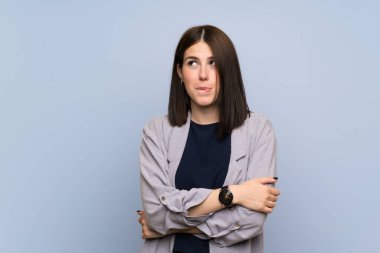 Karışık yüz ifadesi ile izole mavi duvar üzerinde genç kadın