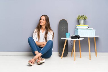 Genç bir kadın yerde oturuyor, yan tarafa bakıyor.